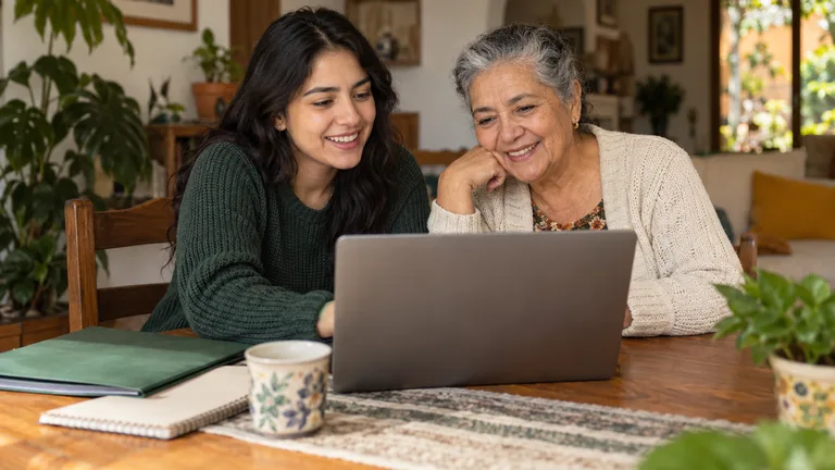 Estudiante y mujer mayor compartiendo una mesa con carpetas y una computadora.